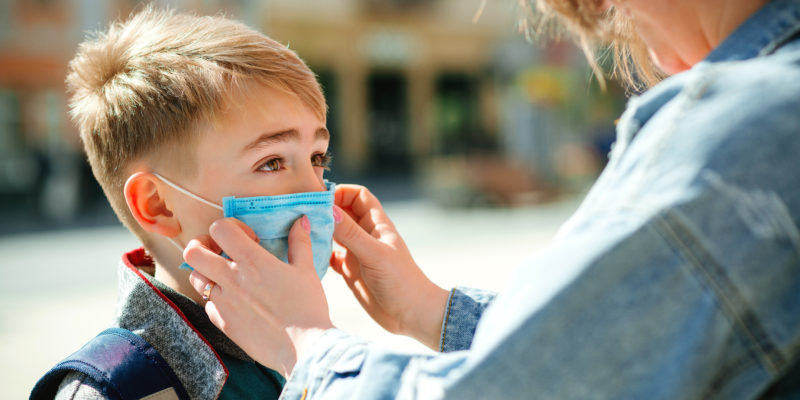 Mother puts a safety mask on her son's face.