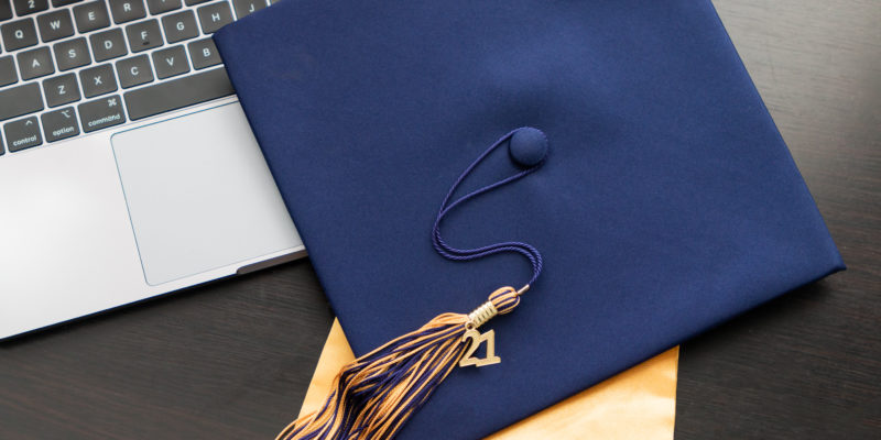 Class of 2021 graduation tassel and cap celebration with a modern computer for virtual learning during covid 19 pandemic.