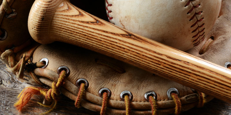 A close up image of an old used baseball, baseball bat, and baseball glove.